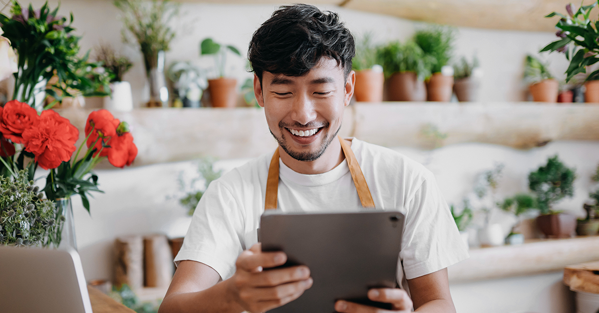 Man smiling, working on a tablet in a plant shop