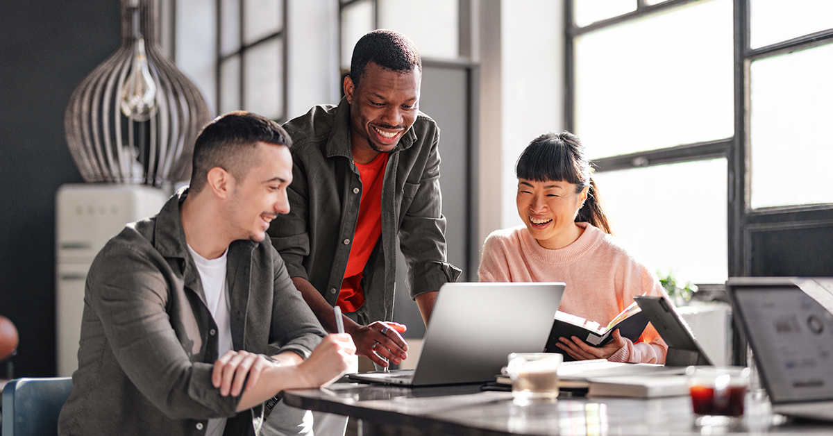 Group of coworkers smiling and reviewing item on laptop