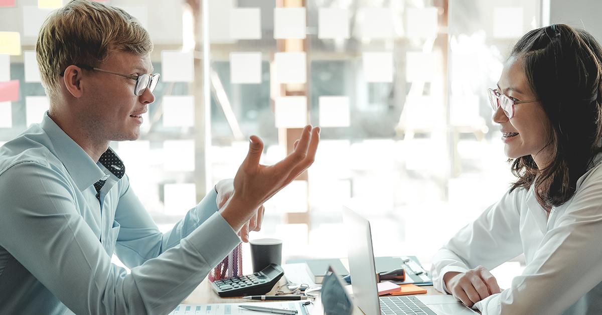 Man and woman sitting at desk and discussing work in bright office