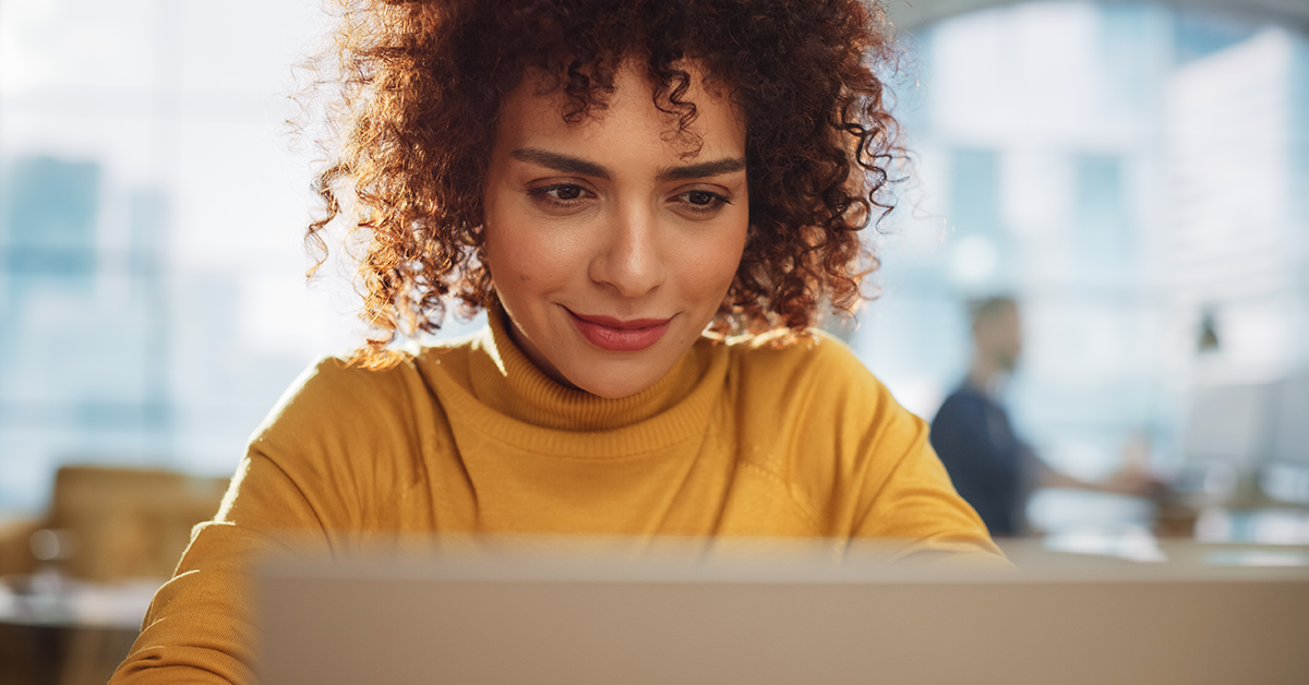 Woman smiling, working behind a laptop
