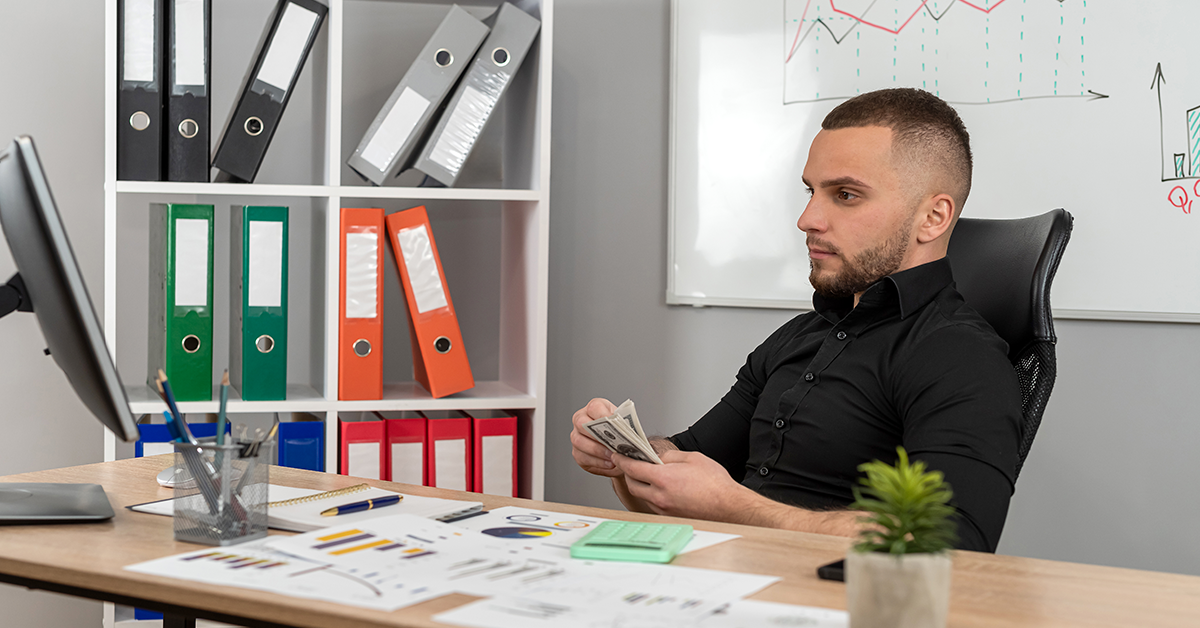 A worker sits at their desk, counting money