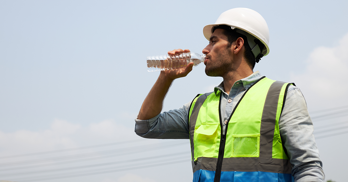 Engineer wearing a hard hat, drinking water on warm summer day
