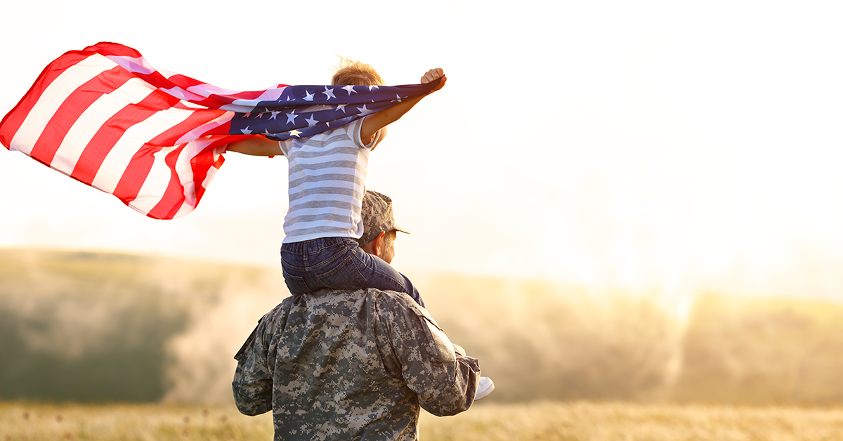 Excited child sitting with american flag on shoulders of father reunited with family