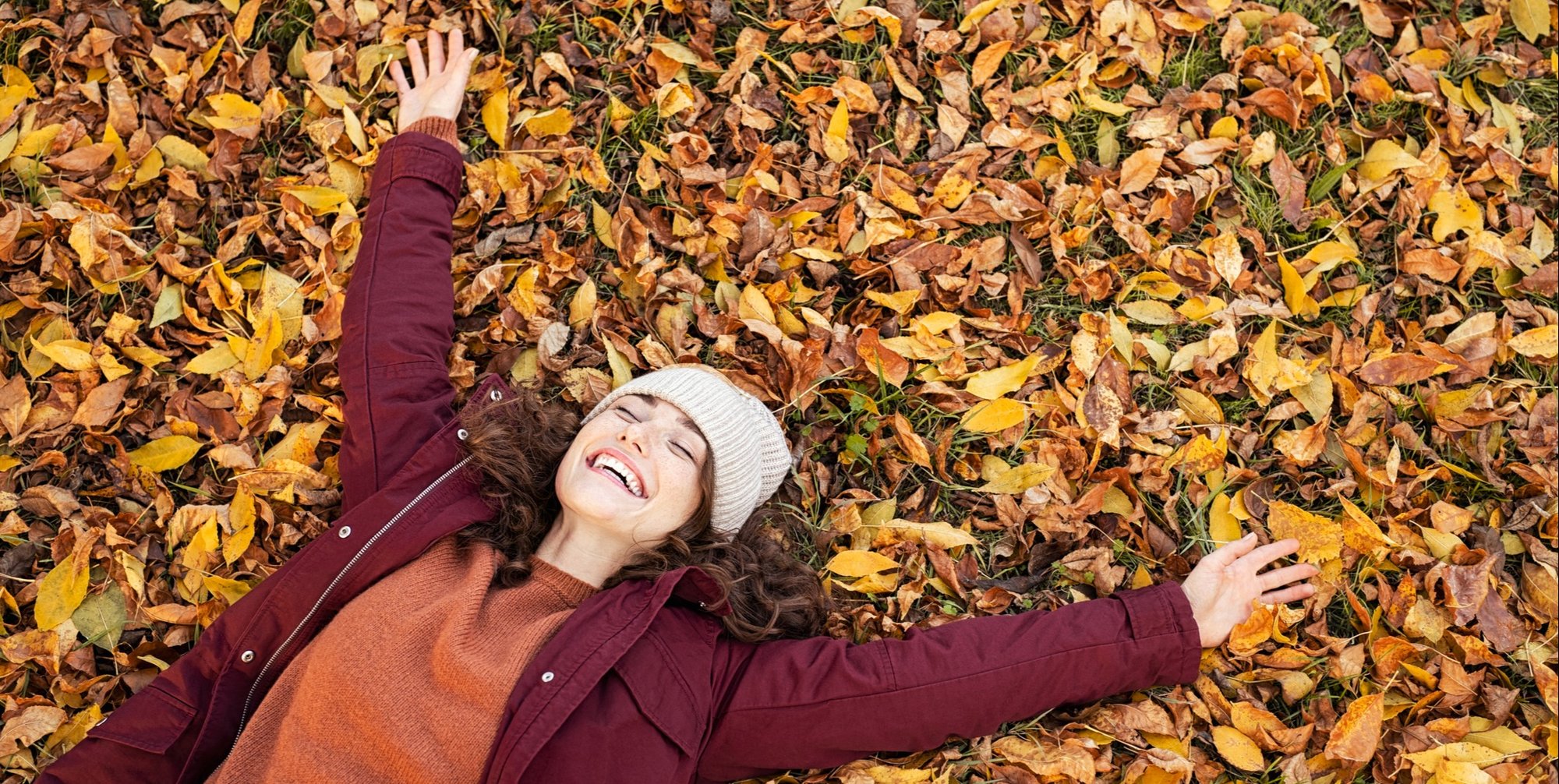 Happy laughing woman lying in a bed of fall leaves