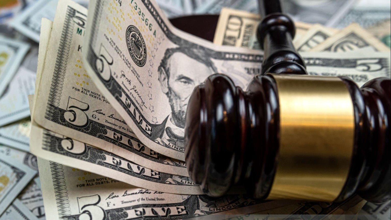 Stack of five dollar bills, gavel lying on top of money