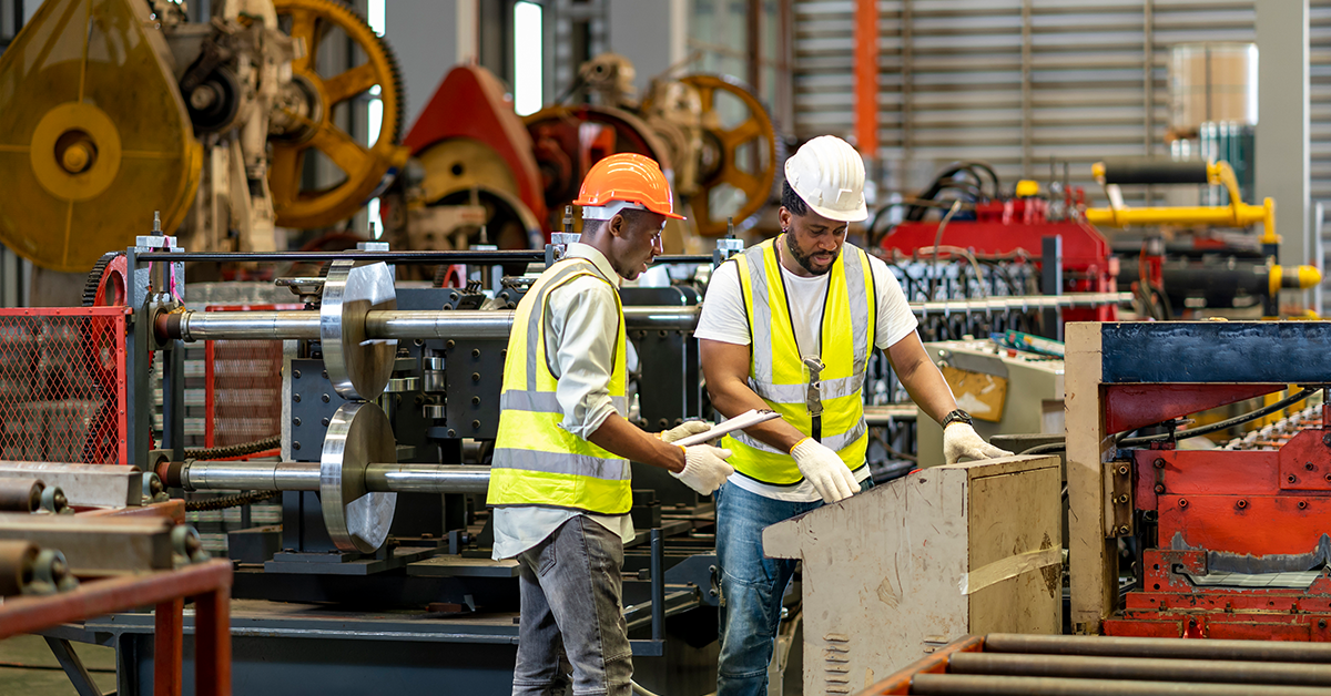 Two male employees working in factory wearing hard hats