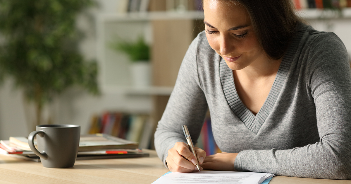 Woman signing document while sitting at desk and working from home.