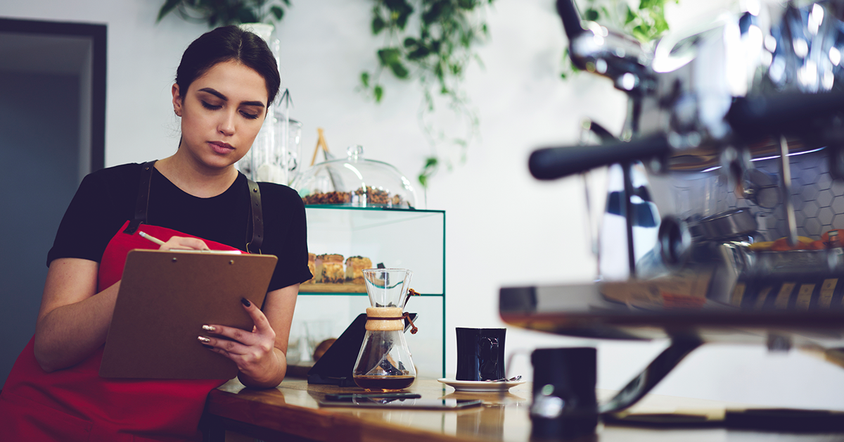 Female barista working in coffee shop, writing on a clipboard