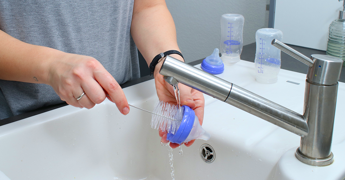 Close up of mothers hands cleaning a baby milk bottle with a brush