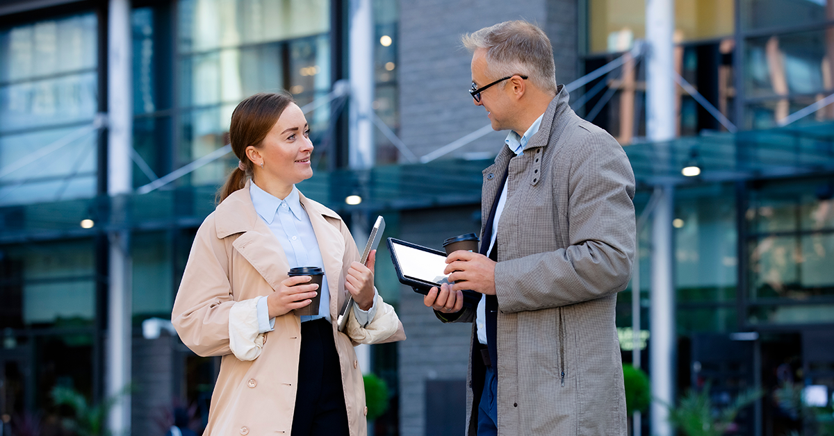 Co-workers discuss ideas outdoors, holding coffee cups
