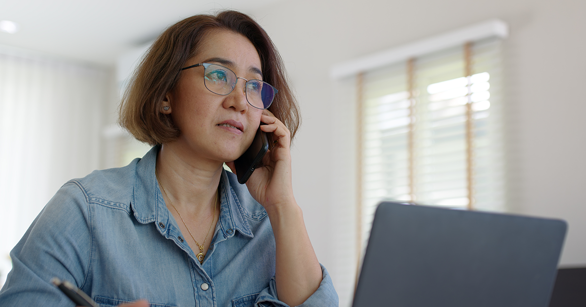 Woman sitting and waiting on a phone call, working on laptop computer at desk home office