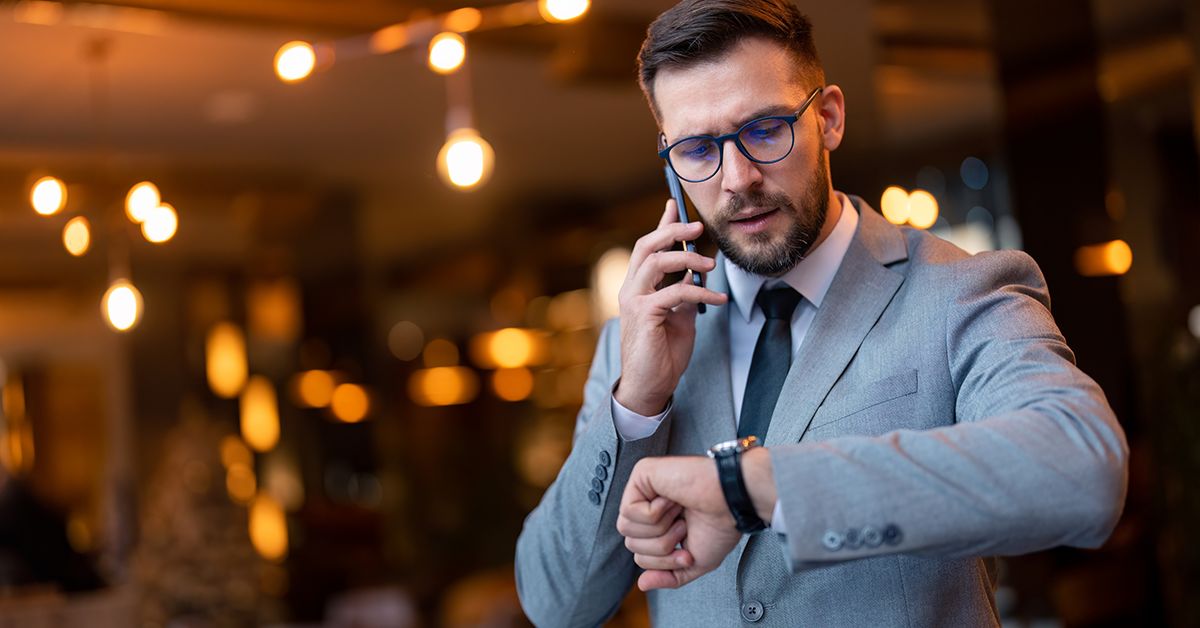 Businessman talking on smartphone, looking at wrist watch checking time