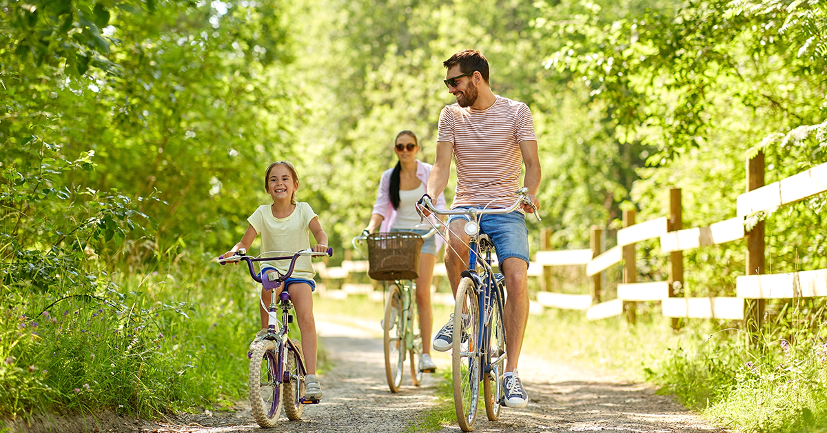 Happy mother, father and daughter riding bicycles in summer park
