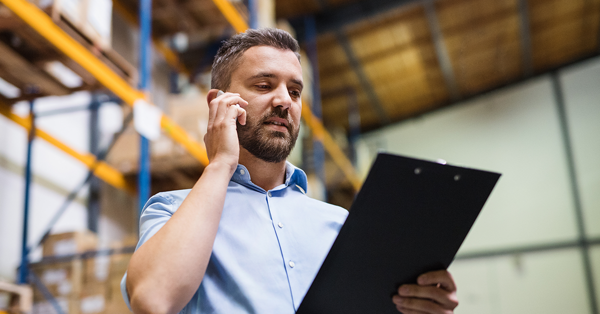 Warehouse supervisor with a smartphone and clipboard