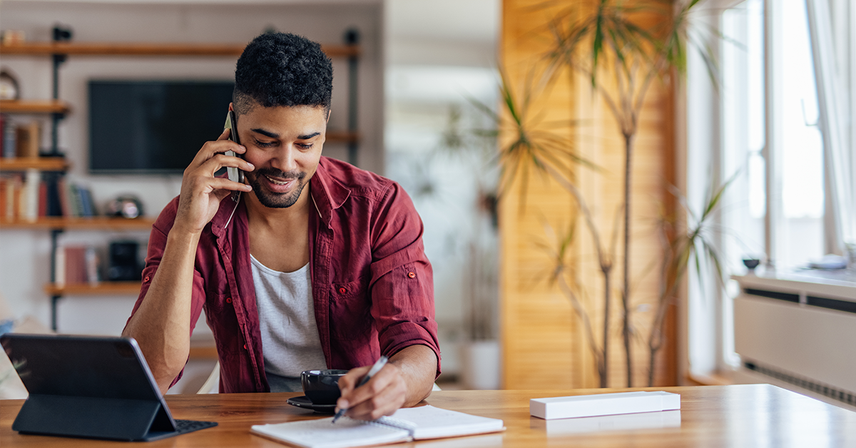 Man at home, taking notes while on a call