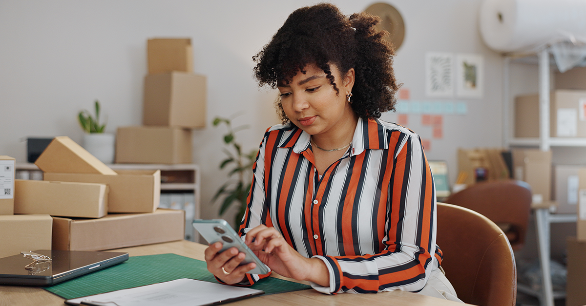 Woman using cell phone in a shipping room with boxes