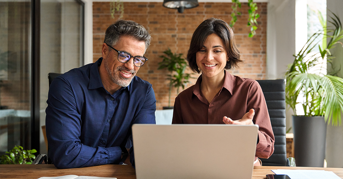 Business man and woman using laptop, working on computer at work desk and having conversation.