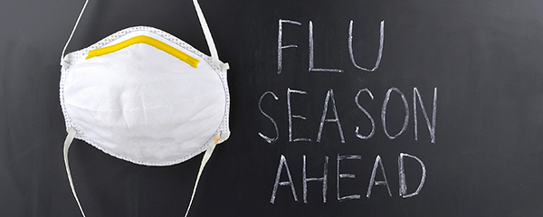 Mask hanging on chalkboard with writing "flu season ahead"