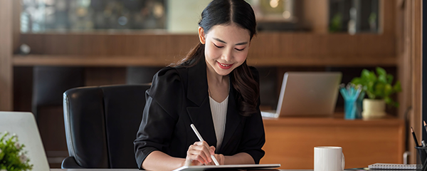 Young businesswoman smiling, sitting, working on tablet in office