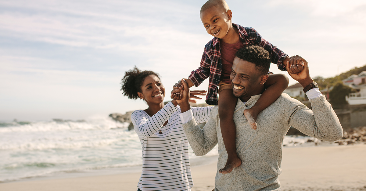 Parents carrying son on shoulders, walking on the beach 