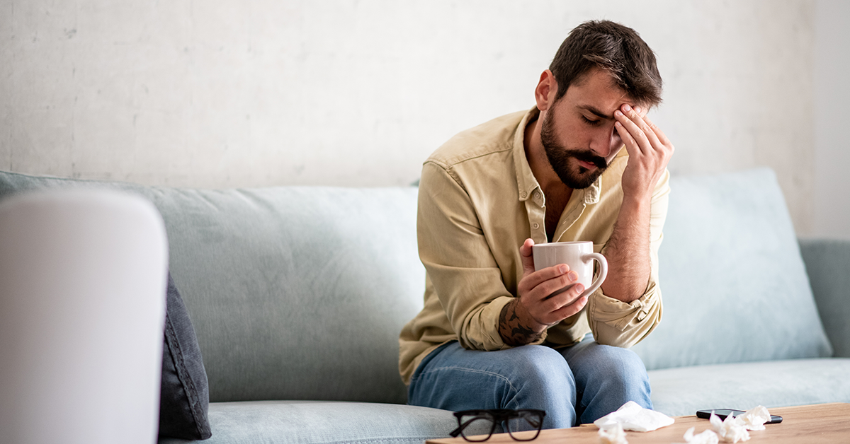 Sick man resting on couch, holding mug